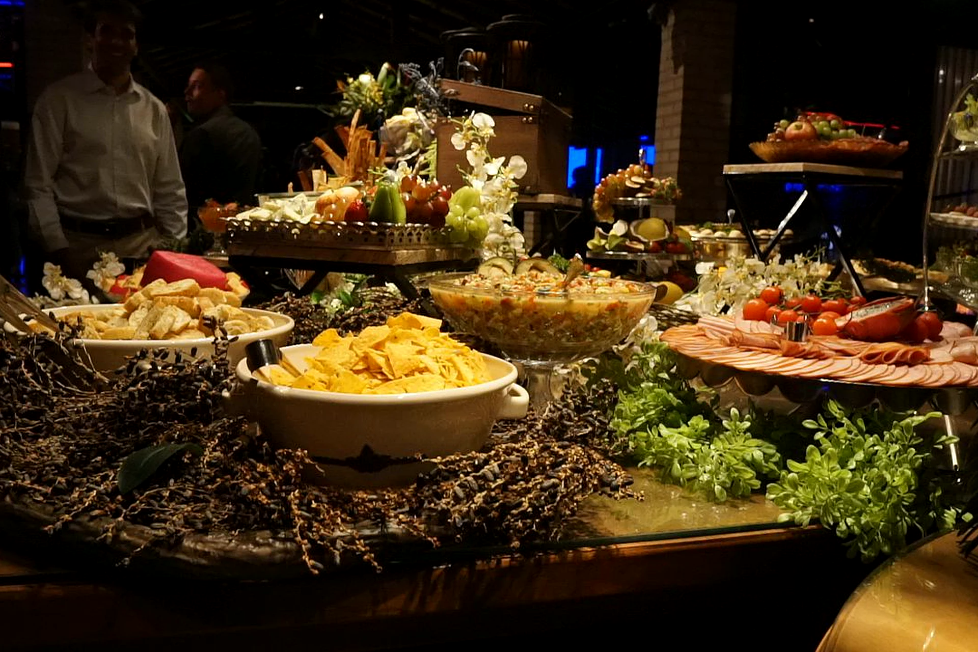 Mesa de buffet com pães, frios e petiscos em evento noturno na Villa do Lago