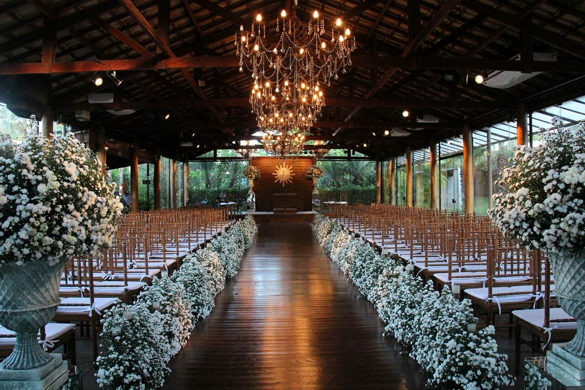 Capela da Villa do Lago com teto de madeira, lustre, cadeiras enfileiradas e corredor com flores brancas