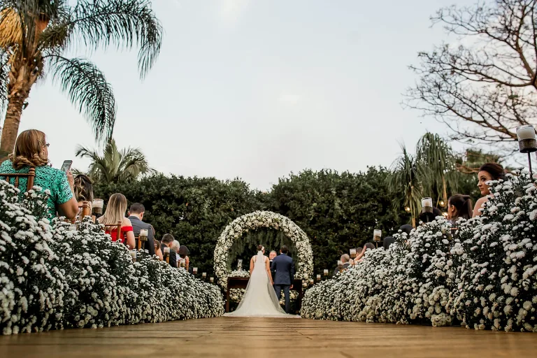 Cerimônia de casamento ao ar livre acontecendo na Villa do Lago, com corredor de flores brancas, convidados e noivos no altar