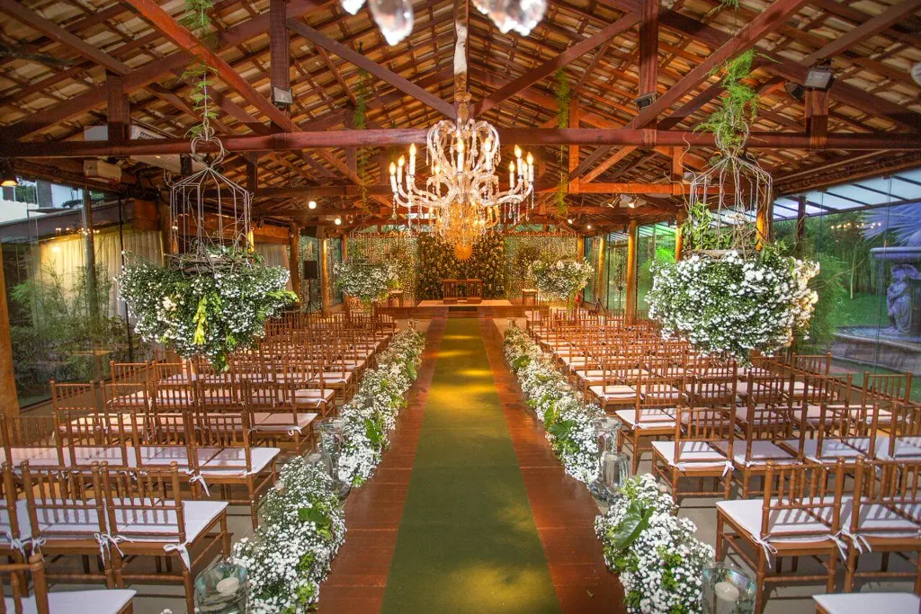Espaço de cerimônias da Villa do Lago de dia, com teto de madeira, fileiras de cadeiras e corredor decorado com flores