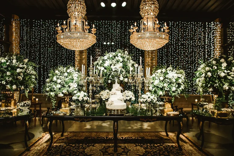 Mesa de doces com lustres de cristal e flores brancas na Villa do Lago