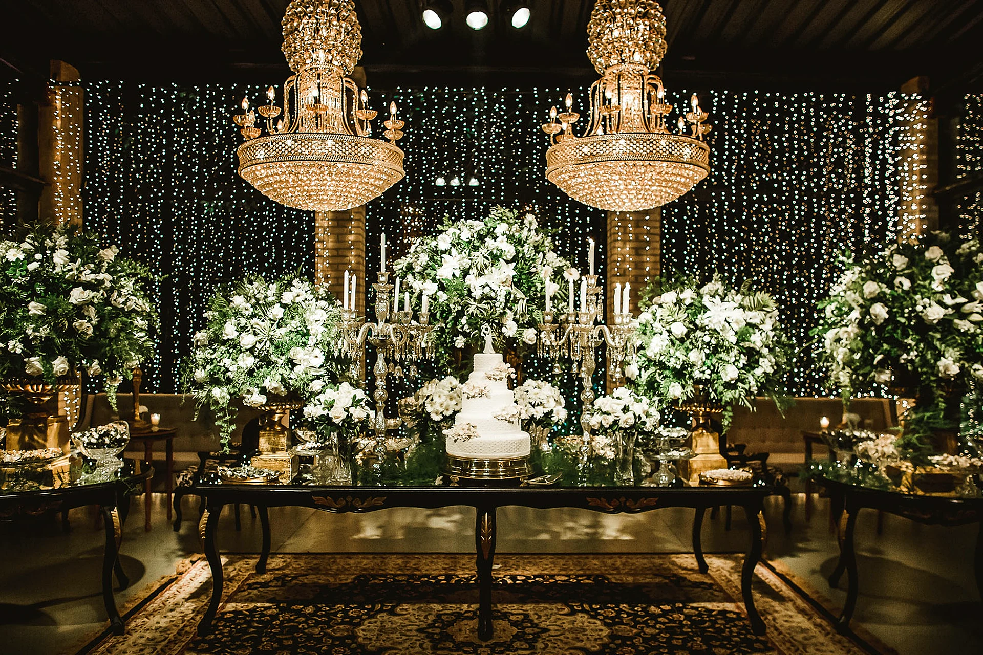 Mesa de doces com lustres de cristal e flores brancas na Villa do Lago