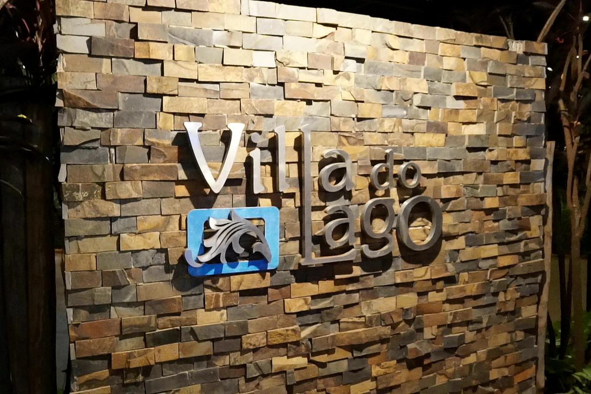 Parede de pedra com o logotipo iluminado da Villa do Lago