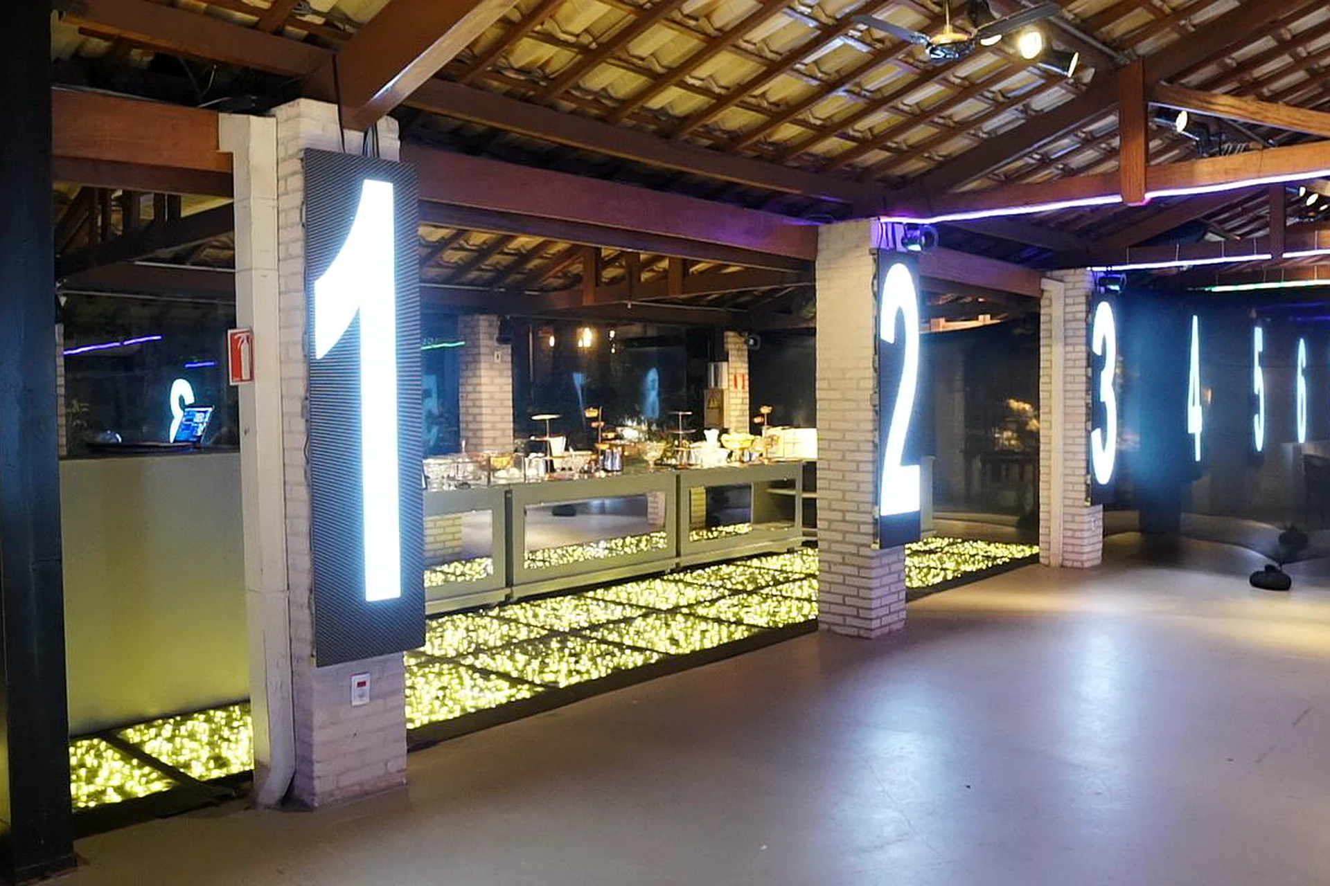 Pista de dança iluminada com colunas numeradas e bar na Villa do Lago